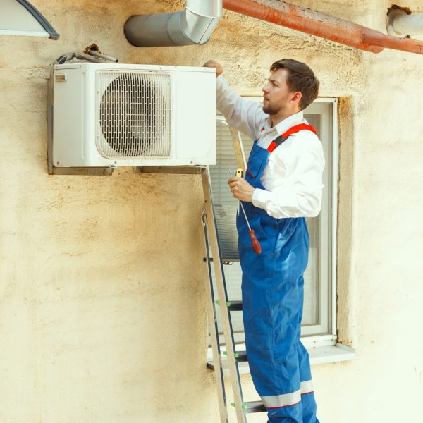 HVAC technician working on a capacitor part for condensing unit. Male worker or repairman in uniform repairing and adjusting conditioning system, diagnosting and looking for technical issues.